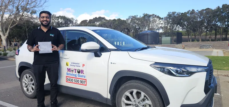 Learner in a black polo holding a certificate beside the school SUV