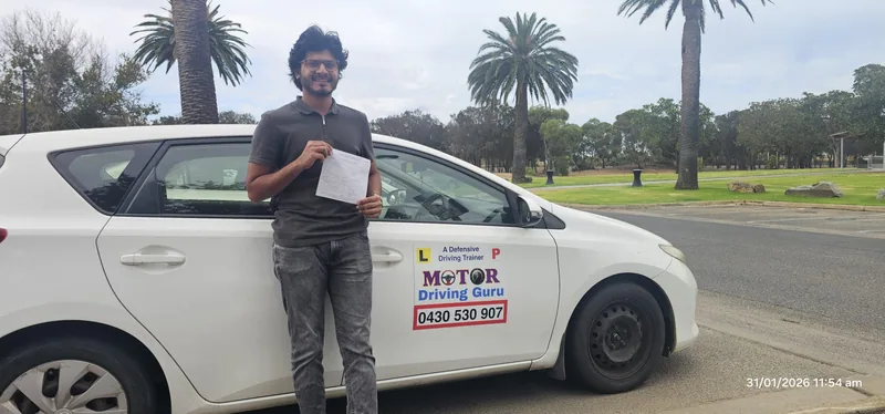 Learner in a dark polo beside the white Motor Driving Guru car