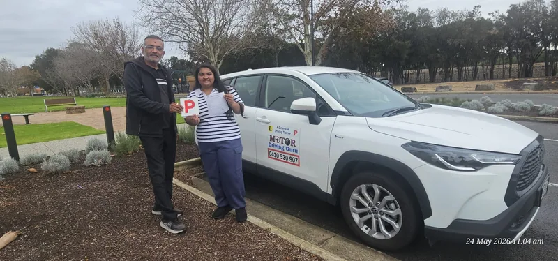 Learner holding a red P plate with her instructor beside the school SUV